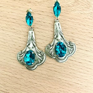May include: A pair of silver dangle earrings with blue teardrop-shaped crystals. The earrings have a detailed, ornate design.