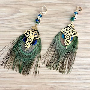 Può includere: Un paio di orecchini pendenti color oro con piume di pavone. Ogni orecchino ha un design in filigrana dorata, perline blu e verdi e una chiusura a leva. Le piume di pavone mostrano sfumature di verde, blu e marrone.