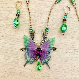 Peut inclure: Un ensemble de collier et boucles d'oreilles délicat avec un pendentif papillon violet et vert, des accents de cristal vert et une chaîne dorée.
