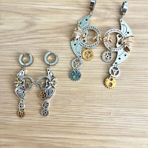 Peut inclure: Boucles d'oreilles de style steampunk avec des croissants de lune argentés, des abeilles dorées et des breloques en forme d'engrenage. Les boucles d'oreilles ont une esthétique industrielle unique, avec un mélange de couleurs métalliques et de détails complexes.