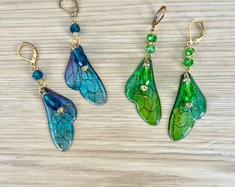 May include: Four pairs of dangle earrings with a fairy wing design. Two pairs are blue and purple, and two are green. Each earring has a gold-coloured hook and is adorned with beads.
