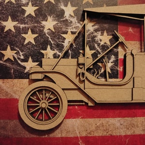 May include: A brown cardboard model of a vintage car, with a steering wheel and a detailed interior, is set against a backdrop of an American flag.