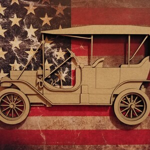 May include: A wooden model of a vintage car with a canvas top, set against a red, white, and blue American flag background.