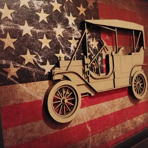 May include: A wooden cutout of a vintage car, painted brown, is displayed against a distressed American flag background. The car has a canvas top and a spare tire on the back.
