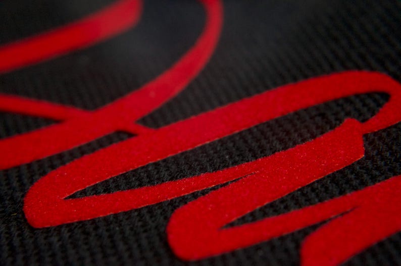 May include: Close-up of a black fabric with a red, stylized word "Raw" printed on it.