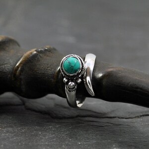 Op de afbeelding: Een zilveren ring met een turquoise steen en ingewikkelde details. De ring is ontworpen om om de vinger te wikkelen.