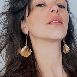 Puede incluir: Una mujer con el pelo largo y castaño oscuro que lleva un vestido de lunares negros y blancos y pendientes grandes de hoja de oro.