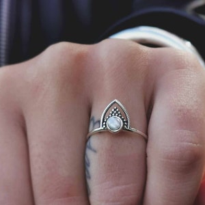 May include: A silver ring with a white stone set in a geometric design. The ring is on a person's finger.