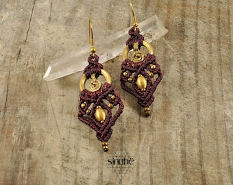 May include: A pair of maroon and gold earrings with a geometric design. The earrings are made with macrame and feature a brass charm.