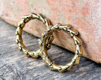 May include: Two circular rings crafted from a metallic gold-toned material, featuring a textured, segmented surface that resembles a series of small, connected nodes or thorns arranged in a continuous, repeating pattern around the band.