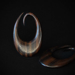 May include: Two wooden ear gauges, one with a curved shape and the other a simple oval, both with a dark brown wood grain.