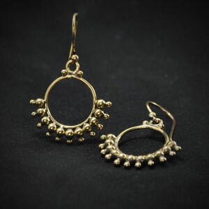 May include: A pair of gold-toned dangle earrings with a circle design. The earrings are made of small beads that are arranged in a circle shape.