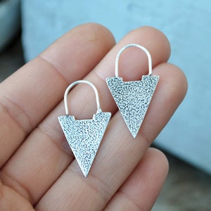 Op de afbeelding: Een paar zilveren driehoekige oorbellen met een textuur. De oorbellen hebben een eenvoudig hoepelontwerp.