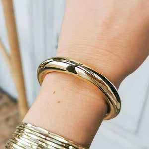 Peut inclure: Un bracelet jonc en or avec une surface lisse et arrondie. Le bracelet est porté au poignet.