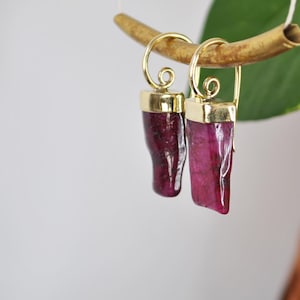 Peut inclure: Une paire de boucles d'oreilles avec des montures dorées et des gouttes de pierres précieuses facettées roses.