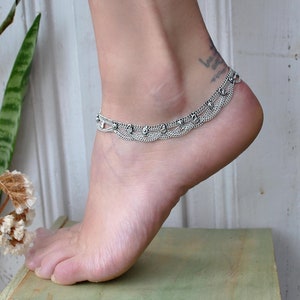 Op de afbeelding: Zilveren enkelband met een delicate ketting en decoratieve bloemmotieven. De enkelband is gemaakt van metaal en heeft een delicaat, vrouwelijk ontwerp.