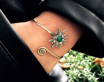 May include: A silver bracelet with a green stone sun design. The bracelet is on a person's wrist.