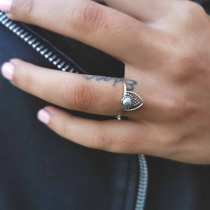 May include: A silver ring with a teardrop-shaped design and a small white stone in the center.