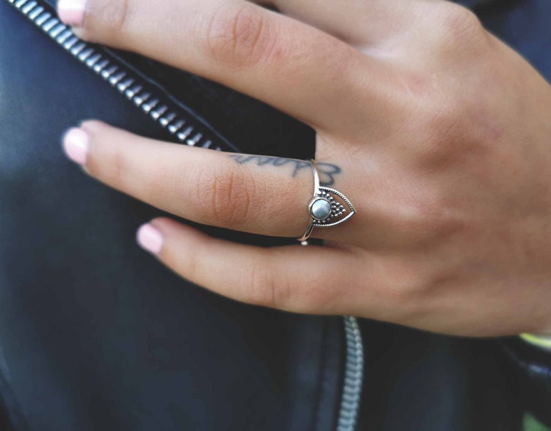 May include: A silver ring with a teardrop-shaped design and a small white stone in the center.
