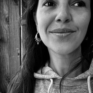 Peut inclure: Une femme aux longs cheveux noirs portant un sweat &agrave; capuche gris. Elle sourit et porte une petite boucle d'oreille argent&eacute;e &agrave; l'oreille gauche.