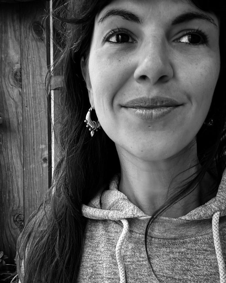 Peut inclure: Une femme aux longs cheveux noirs portant un sweat &agrave; capuche gris. Elle sourit et porte une petite boucle d'oreille argent&eacute;e &agrave; l'oreille gauche.