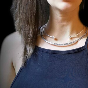 May include: A silver choker necklace with a delicate chain and two small round accents. The necklace is layered over a thicker silver chain with a textured design.