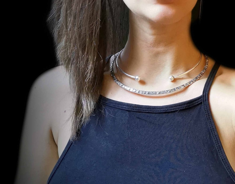 May include: A silver choker necklace with a delicate chain and two small round accents. The necklace is layered over a thicker silver chain with a textured design.
