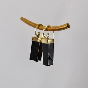 Puede incluir: Un par de pendientes de &oacute;nix negro con detalles dorados. Los pendientes son de forma rectangular y tienen un acabado pulido.