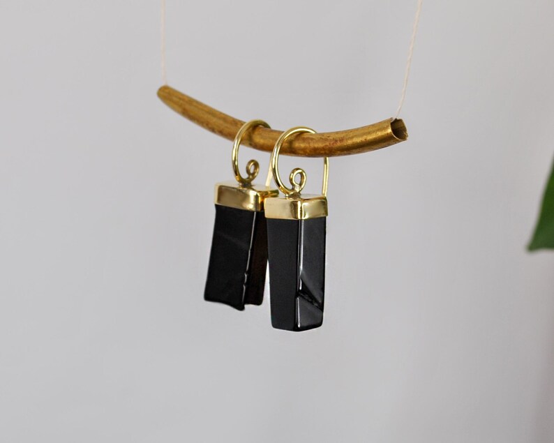 Puede incluir: Un par de pendientes de &oacute;nix negro con detalles dorados. Los pendientes son de forma rectangular y tienen un acabado pulido.