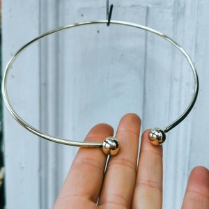 May include: A gold choker necklace with two round ball accents.