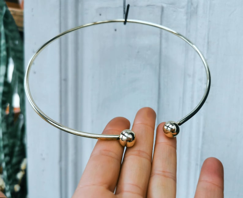 May include: A gold choker necklace with two round ball accents.