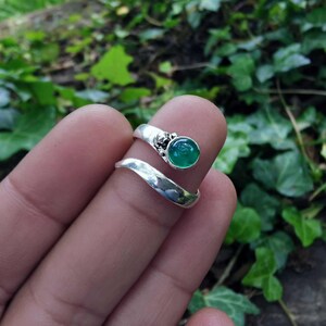 Op de afbeelding: Een zilveren ring met een groene edelsteen gezet in een decoratieve zilveren setting. De ring is ontworpen om om de vinger te wikkelen.