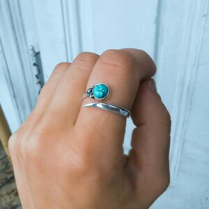 Op de afbeelding: Een zilveren ring met een turquoise steen in een bloemmotief. De ring is open en wikkelt zich om de vinger.