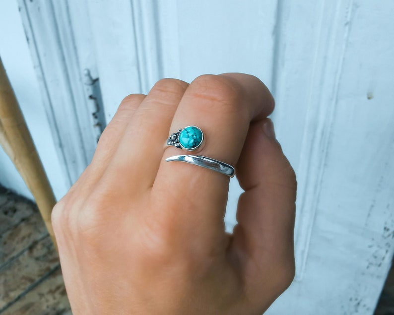Op de afbeelding: Een zilveren ring met een turquoise steen in een bloemmotief. De ring is open en wikkelt zich om de vinger.