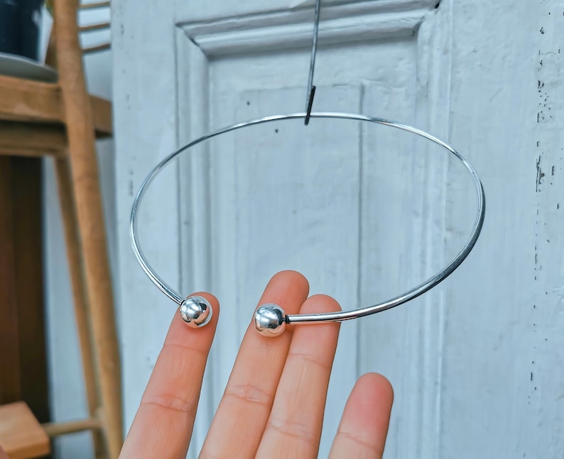 May include: A silver choker necklace with two round balls at the ends.