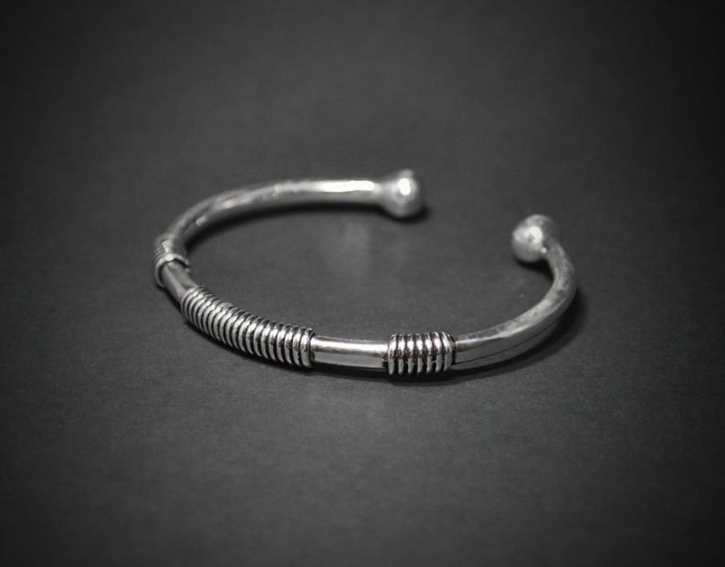 May include: A silver cuff bracelet with a textured finish. The bracelet has a coiled wire design in the centre and rounded ball ends. The open design allows for easy wear. This piece is a stylish accessory.