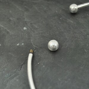 May include: A silver bangle bracelet with two round silver beads. The bracelet is open and has a screw closure.