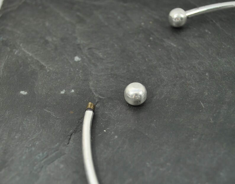 May include: A silver bangle bracelet with two round silver beads. The bracelet is open and has a screw closure.