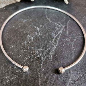 May include: A silver bangle bracelet with two round balls at the ends.