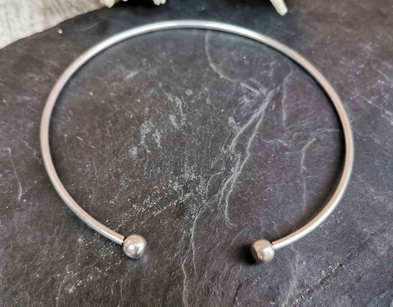 May include: A silver bangle bracelet with two round balls at the ends.