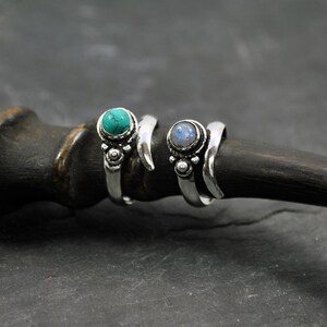 Op de afbeelding: Twee zilveren ringen met edelsteen accenten. De ring aan de linkerkant heeft een turquoise steen, terwijl de ring aan de rechterkant een blauwe maansteen heeft.