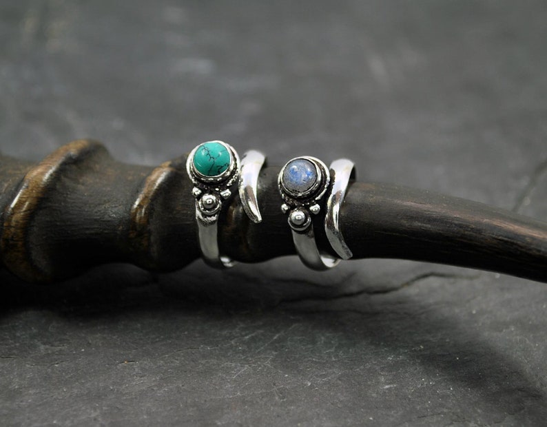 Op de afbeelding: Twee zilveren ringen met edelsteen accenten. De ring aan de linkerkant heeft een turquoise steen, terwijl de ring aan de rechterkant een blauwe maansteen heeft.