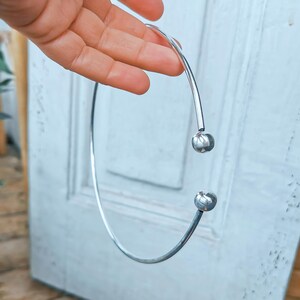 May include: A silver choker necklace with two round metal balls at the ends.