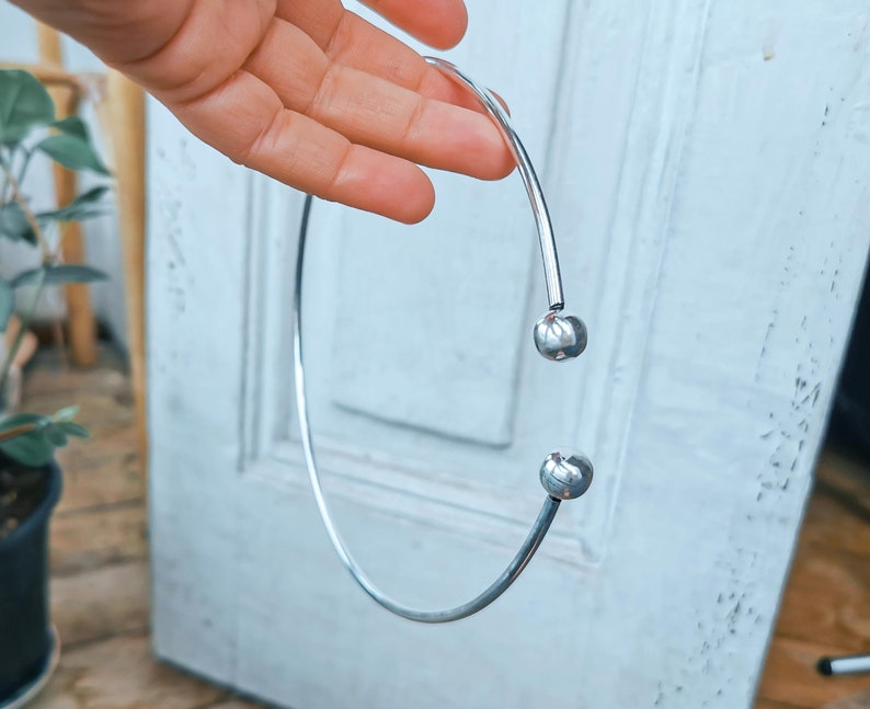 May include: A silver choker necklace with two round metal balls at the ends.