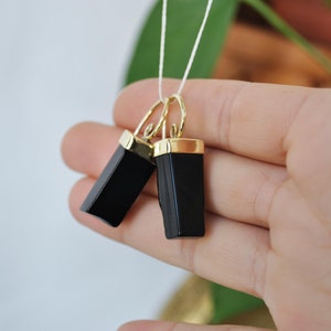 Puede incluir: Un par de pendientes de &oacute;nix negro con detalles dorados. Los pendientes son de forma rectangular y tienen un acabado pulido.