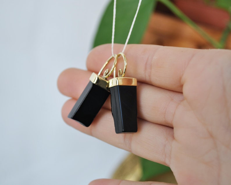 Puede incluir: Un par de pendientes de &oacute;nix negro con detalles dorados. Los pendientes son de forma rectangular y tienen un acabado pulido.