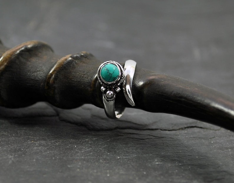 Op de afbeelding: Een zilveren ring met een turquoise steen en ingewikkelde details. De ring is ontworpen om om de vinger te wikkelen.