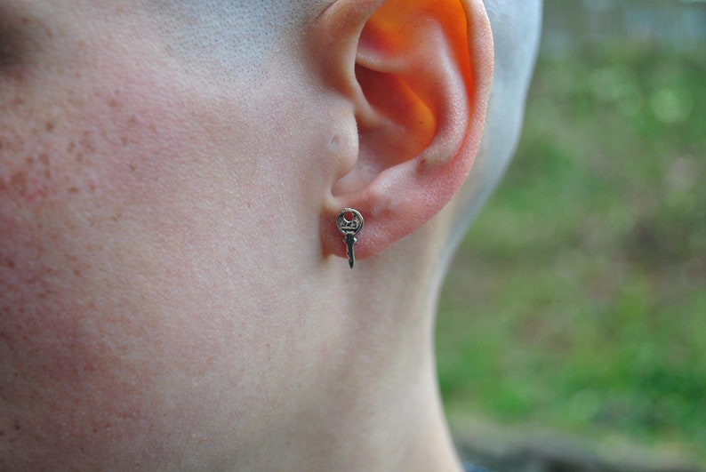 May include: A silver key-shaped earring with a small, detailed design.