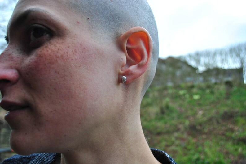 May include: Close-up of a person's face with a shaved head and a small stud earring in their left ear.