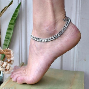 Könnte beinhalten: Ein silberfarbenes Fußkettchen mit einer Kette und kleinen, muschelförmigen Anhängern. Das Fußkettchen wird am Knöchel getragen und zeigt sein filigranes Design. Ein stilvolles Accessoire.